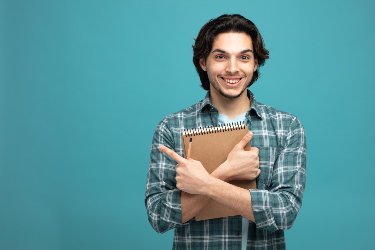 smiling-young-handsome-man-holding-note-pad-pencil-looking-camera-pointing-side-isolated-blue-background-with-copy-space