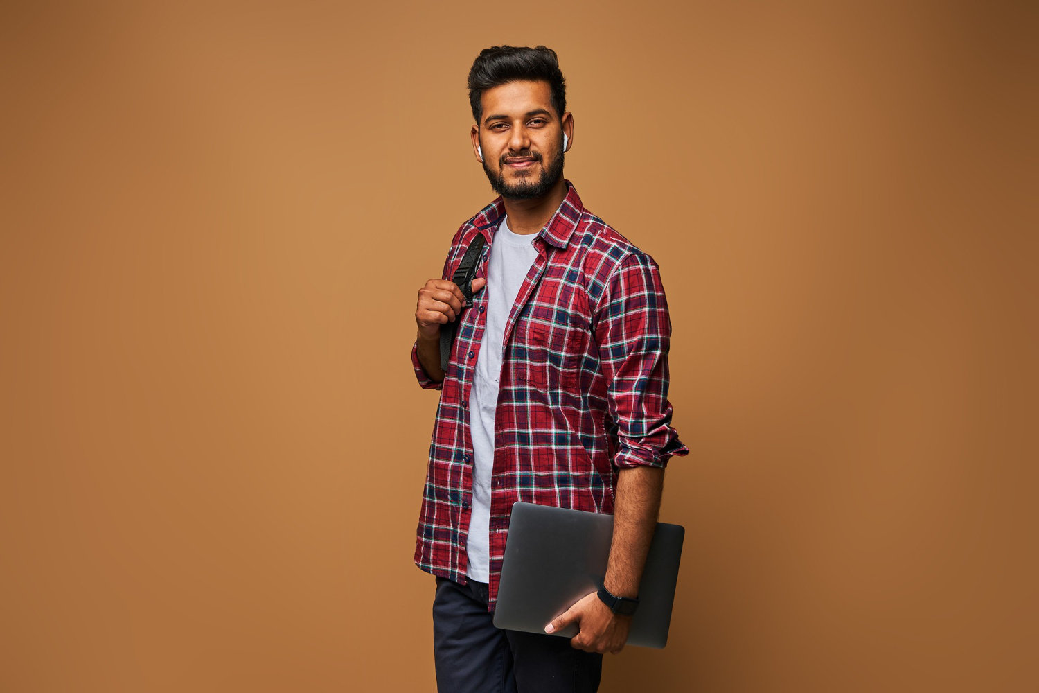 smiling-indian-man-casual-close-with-laptop-backpack-pastel-wall